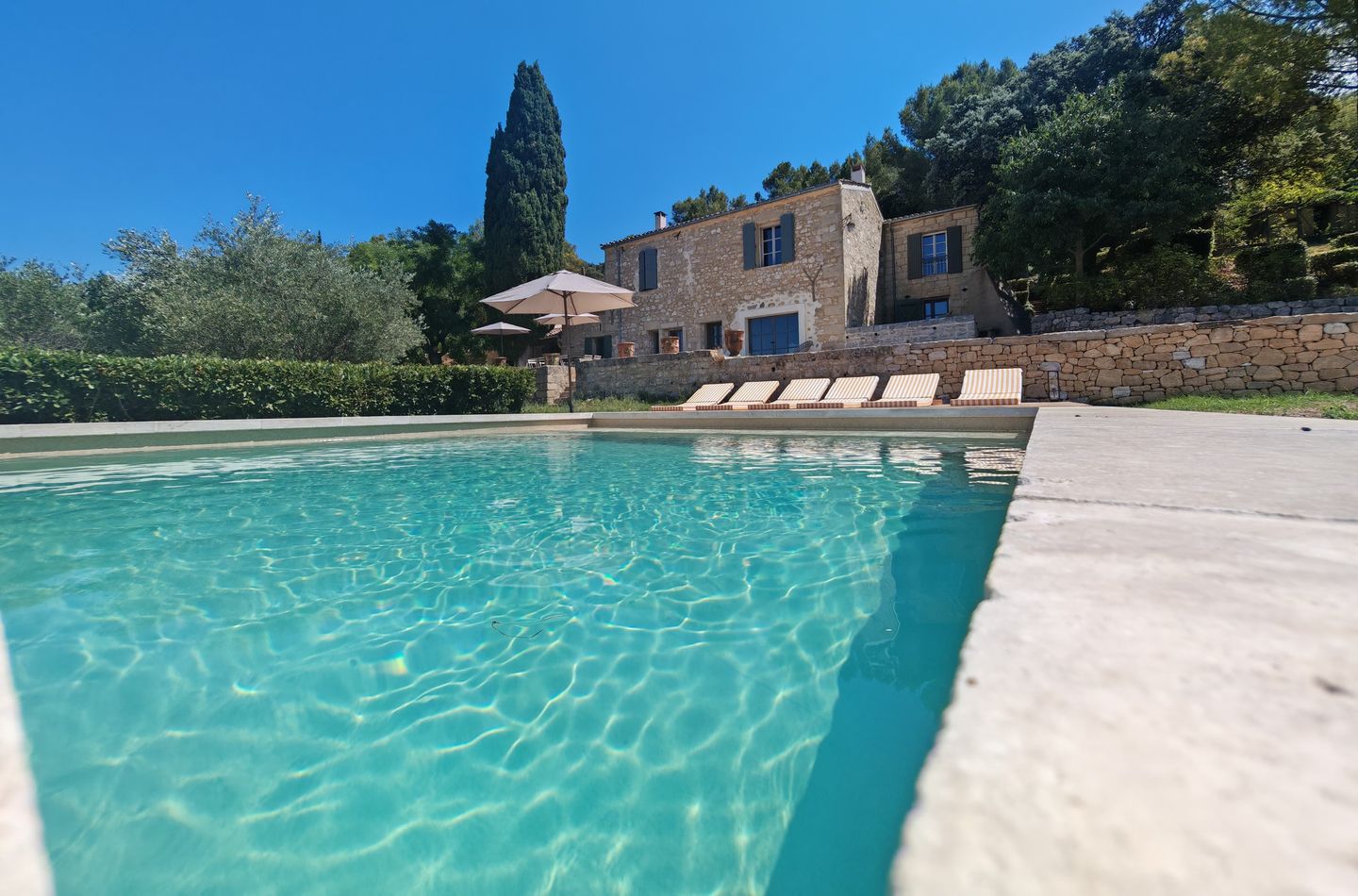 Piscine à l'eau turquoise au pied d'une maison en pierre, entre oliviers et cyprès